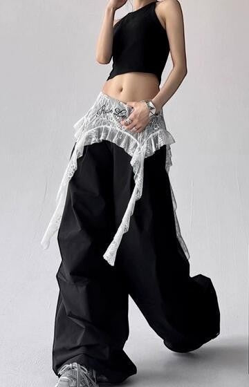 Renkaのアシンメトリーなシースルーレースレイヤリングミニスカート。ウエストで結ぶデザインで、黒のワイドパンツの上に重ね着しています。